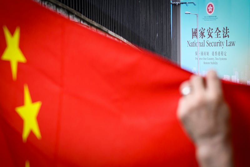 A June 26, 2020, image shows a billboard referring to the then incoming Hong Kong National Security Law as a Chinese flag is held up by a pro-China activist during a rally in Hong Kong.
